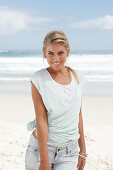 A blonde woman on the beach wearing a light t-shirt and denim shorts