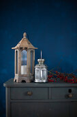 Lanterns and branch of red berries on top of chest of drawers