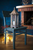 Lantern and branch of berries on wooden chair with fairy lights on floor