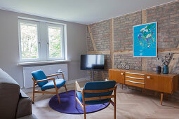 TV, sideboard and two chairs in living room with brick wall