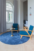 Blaue Sessel und Beistelltisch auf rundem Teppich vor Fenster