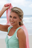 A blonde woman on a beach with a scarf and a turquoise top