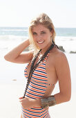 A young blonde woman on a beach wearing a striped swimsuit