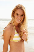 A blonde woman on a beach wearing a white and yellow bikini