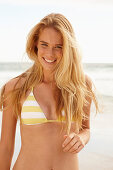 A blonde woman on a beach wearing a white and yellow bikini