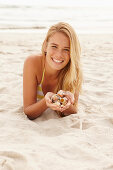 A blonde woman lying on a beach with shells