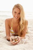 Blonde Frau mit Muschelschalen am Strand liegend