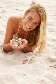 A blonde woman lying on a beach with shells