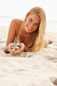 Blonde Frau mit Muschelschalen am Strand liegend