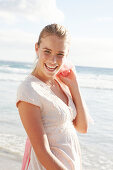 A blonde woman by the sea wearing a white embroidered dress