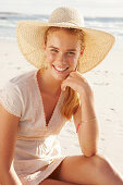 A blonde woman by the sea wearing a white dress and a hat