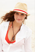 A brunette woman wearing a hat, a red bikini top and a white blouse
