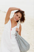 Brünette Frau in weißem Sommerkleid mit Tasche am Strand