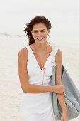 A brunette woman by the sea with a bag wearing a white summer dress