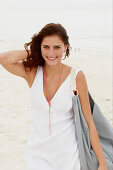 A brunette woman by the sea with a bag wearing a white summer dress