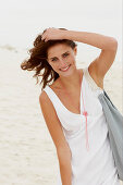 A brunette woman by the sea with a bag wearing a white summer dress