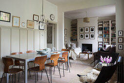 Dining table against panelled wall and seating area around fireplace flanked by fitted bookshelves