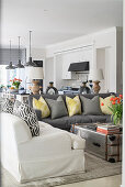 Weißes und graues Sofa mit Kissen und Metallkoffer als Couchtisch in offenem Wohnraum