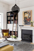 Coffee table and classic chair in front of fireplace and bookcase with ladder in living room