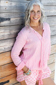 Reife Frau in rosa Bluse und rosa Shorts vor Holzwand