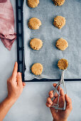 Woman placing cookie balls on a baking sheet using an ice cream scooper