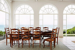 Long table with wooden chairs in front of arched window fronts with sea view