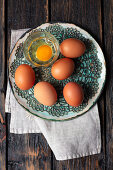 Frische braune Eier und ein aufgeschlagenes Ei im Glas
