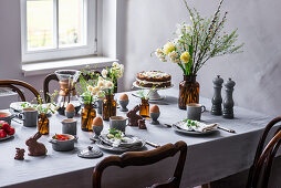 Gedeckter Tisch zum Osterfrühstück mit gekochten Eiern, Kaffee, Möhrentorte, Schokoladenhasen und Obstsalat
