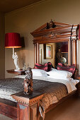 Grand mahogany bed with mirrored headboard in bedroom with red lampshades