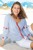 A blonde woman outside wearing a blue-and-white striped blouse and shorts