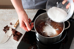 Cooking chocolate being added to a pot with sugar and water