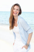 A young woman by the sea wearing a white top and a light blue shirt