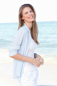 A young woman by the sea wearing a white top and a light blue shirt