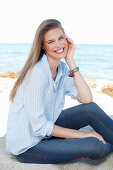 A young woman by the sea wearing a light blue shirt and jeans