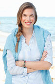 Junge Frau in hellblauem Hemd und Pullover am Meer