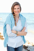 Junge Frau in hellblauem Hemd, Pullover und Jeans am Meer