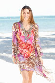 A brunette woman by the sea wearing a colourful beach dress