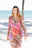 A brunette woman by the sea wearing a colourful beach dress