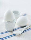 A breakfast egg in an eggcup on a blue and white striped cloth napkin