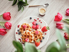 Dish with delicious waffles and fresh berries between red tulips on board