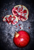 A whole pomegranate and a split pomegranate on a grey metal surface