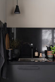 Sink in kitchen with dark grey cupboards and black splashback