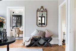 Cushions on upholstered stools below antique mirror on wall and view into dining room