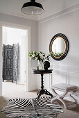 Antique table, upholstered stool, zebra-skin rug and round mirror