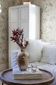 Leafy branches in china vase on stacked magazines on wooden table in living room