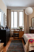 Black chest of drawers, desk and bed with colourful bedspread in bedroom