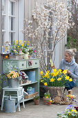 Easter terrace with rock pear, daffodils, planted box and zinc bucket, woman with wooden Easter bunny