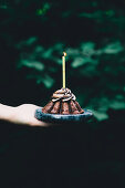 A hand holding a chocolate espresso cake with a birthday candle