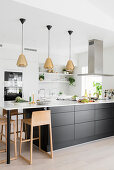 White, open-plan kitchen with three pendant lamps above black kitchen counter