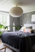 Collection of scatter cushions on double bed and lamp with fluffy lampshade in bedroom with grey walls